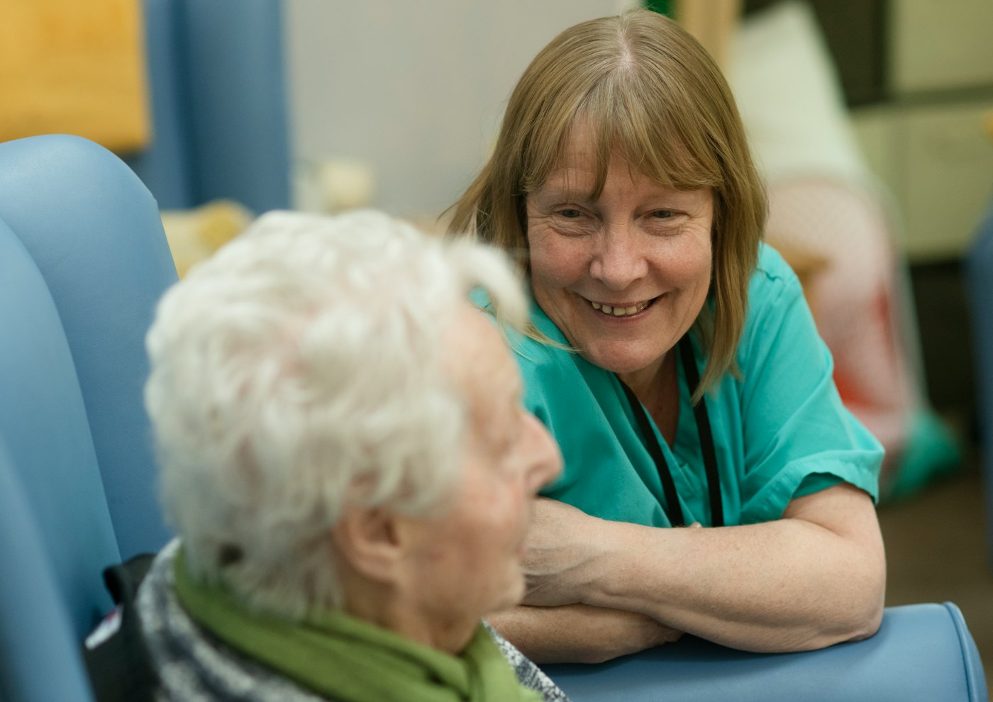 Caregiver leaning toward an elderly person in a chair